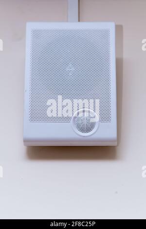 Un émetteur radio blanc est fixé sur un mur beige. Sur la face avant se trouve une grille avec de petits trous pour un haut-parleur. Appareil électronique pour écouter des messages, de la musique et des actualités. Banque D'Images