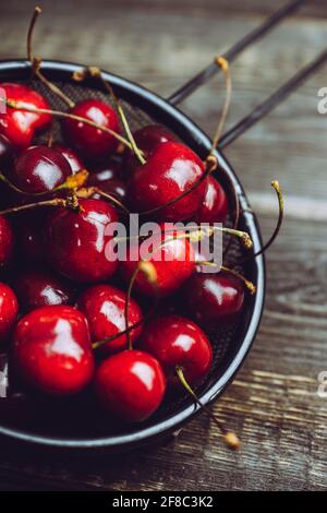 Cerises mûres et juteuses en passoire en métal noir sur fond rustique foncé. Mise au point sélective. Faible profondeur de champ. Banque D'Images