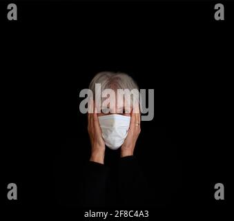 Femme plus âgée coup de tête portant un masque facial coronavirus, tête dans les mains. Désespoir, stress concept sur fond noir. Banque D'Images