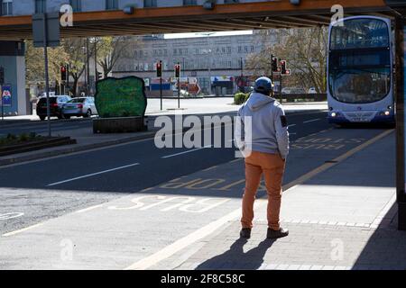 Un homme dans un centre-ville attend un bus à un arrêt de bus Banque D'Images