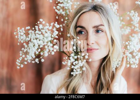 Portrait en gros plan d'une charmante femme heureuse d'humeur printanière avec des fleurs de gitsophila sur sa tête. Portrait de style de vie d'une femme confiante dans sa trentaine. Banque D'Images