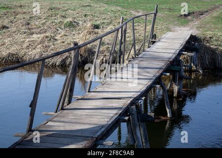 Vieux pont en bois sur une rivière. Pont en ruine. Supports détruits. Rivière étroite dans un champ. Jour ensoleillé. Façon terrible Banque D'Images