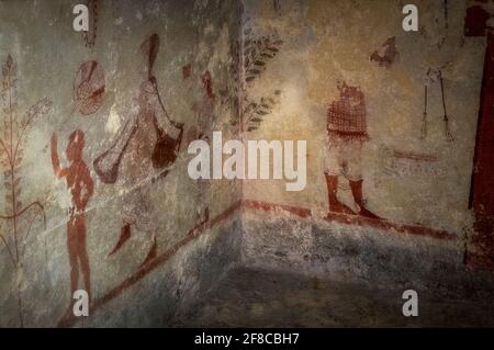 Une danseuse de haut-marche portant une robe longue à manches larges et des chaussures pointues, précédée d'un jeune enfant portant un flabellum décoratif ou un ventilateur, Sont parmi les personnages peints il y a environ 2 500 ans sur le mur gauche de la tombe de Cardarelli dans la nécropole de Monterozzi de l'ancienne ville de Tarchuna ou Tarchna à Tarquinia, Latium, Italie. Le tombeau, trouvé en 1959, est dédié au poète et journaliste Vincenzo Cardarelli (1887-1959), né à Corneo, le nom de Tarquinia jusqu'en 1922. Banque D'Images