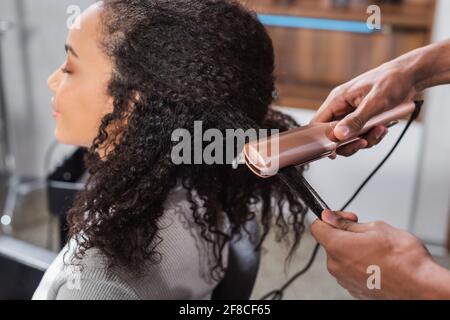 Coiffeur afro-américain utilisant un lisseur de cheveux sur le client Banque D'Images