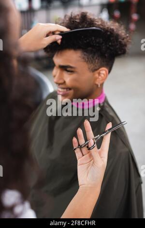 Ciseaux à la main de coiffeur afro-américain peignant le client sur arrière-plan flou Banque D'Images