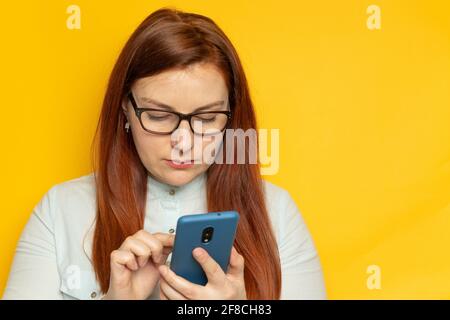 Une femme d'affaires ciblée utilise un smartphone tout en se tenant contre un mur jaune arrière-plan Banque D'Images