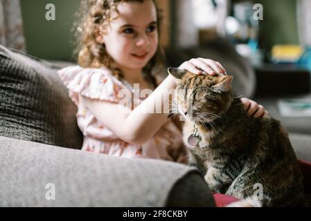 Petite fille jouant avec son chat sur le canapé dedans le salon