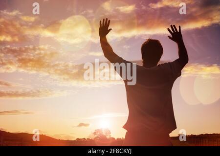 Silhouette d'un homme avec les mains posées dans le concept de religion, coucher de culte, de prière et de louange Banque D'Images