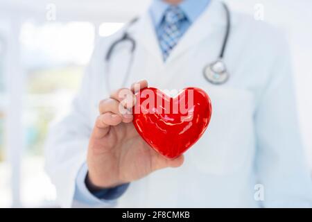 Médecin ou cardiologue tenant le cœur avec soin dans les mains à concept de cabinet hospitalier pour les soins de santé et le diagnostic de pouls cardiaque médical test Banque D'Images