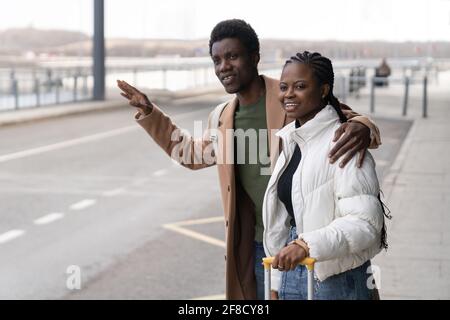 Transfert du terminal: couple africain près de l'aéroport avec main levée essayer de prendre un taxi après l'arrivée Banque D'Images