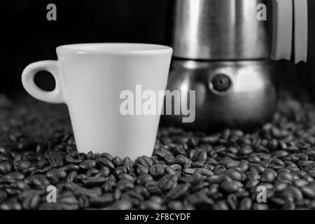 Photo en noir et blanc avec une machine à espresso italienne, grains de café et une tasse blanche sur fond sombre. Banque D'Images