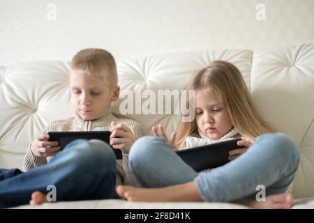 Deux petits enfants, garçon et fille, tenant une tablette et regardant des dessins animés à la maison. Frère et sœur s'amusant avec un appareil numérique assis sur un canapé. Banque D'Images