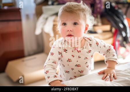 enfant avec les yeux effrayés se tient au lit. fille de 1 ans apprend à marcher et a peur de prendre une mesure Banque D'Images