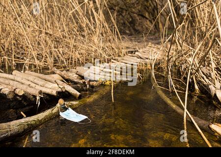 Masque médical dans l'eau claire de la petite rivière forestière flottant près du pont en bois. Banque D'Images