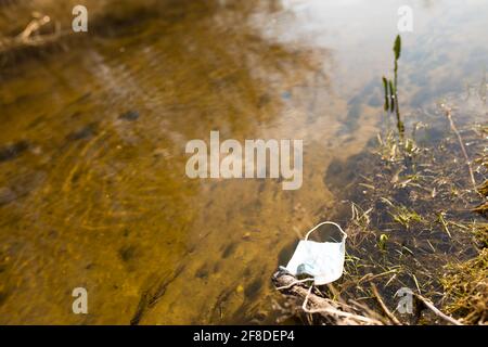 Utilisé masque médical dans une eau de petite rivière, jour ensoleillé avec espace de copie. Banque D'Images