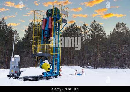 Vérin vertical de pompe à huile fonctionnant en hiver. Au coucher du soleil orange à l'aube du ciel avec des nuages. Machine industrielle d'énergie de plate-forme pétrolière pour le pétrole au coucher du soleil Banque D'Images