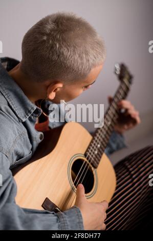 Jeune femme blonde à poil court apprenant à jouer de la guitare acoustique sur fond blanc. Banque D'Images