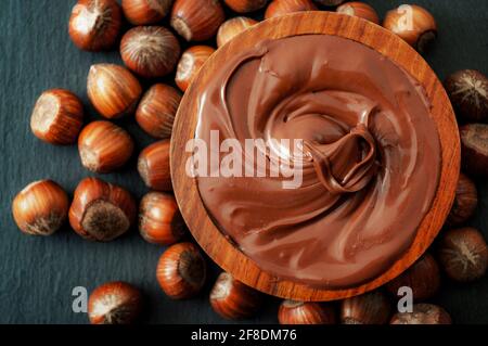 Le thème du petit déjeuner, du dessert classique et des sucreries rustiques est composé d'un bol en bois brun de chocolat fondu au chocolat noisette entouré de noisettes crues Banque D'Images