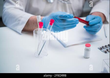 Gros plan d'un tube à essai médical dans les mains d'un médecin en gants de latex à son bureau. Bureau de l'investigateur médical. Banque D'Images