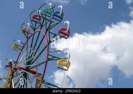 Les familles s'amusent à monter, descendre et faire le tour d'un ferris haut en couleur à travers un skiy bleu et des nuages par une journée d'été Banque D'Images