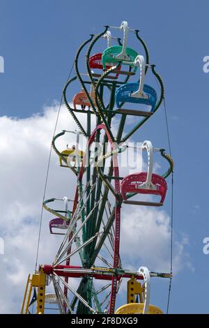 Les familles s'amusent à monter, descendre et faire le tour d'un ferris haut en couleur à travers un skiy bleu et des nuages par une journée d'été Banque D'Images