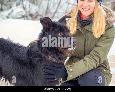 Jeune femme jouant avec drôle chien d'animal de compagnie noir avec la neige. Sur l'arrière-plan. Jouer avec la neige. Adorable chien appréciant son temps, l'hiver. Copier l'espace Banque D'Images