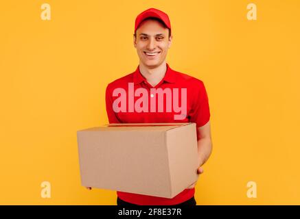 Image d'un jeune messager heureux dans Red Hat debout avec boîte aux lettres isolée sur fond jaune Banque D'Images