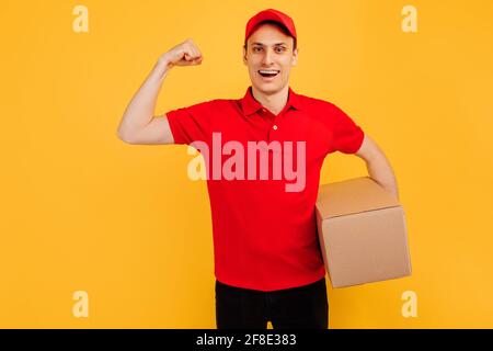 Image d'un jeune messager heureux dans Red Hat debout avec boîte aux lettres isolée sur fond jaune Banque D'Images