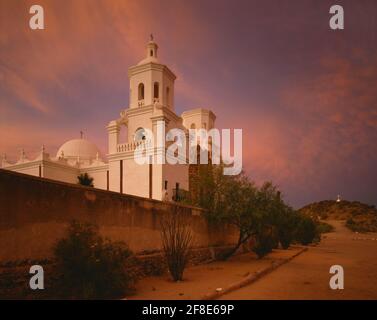 Tohono O'odham Indian Reservation Pima County AZ / MAI ciel rouge au crépuscule au-dessus de la mission Kino de San Xavier avec colline et traverser au-delà. Banque D'Images