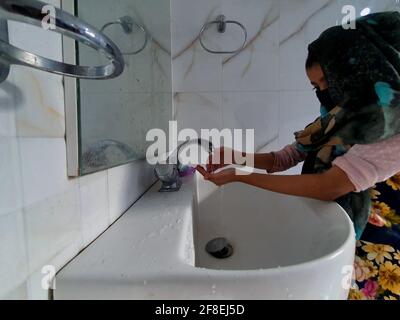 Se laver les mains dans la salle de bains par des enfants masqués pendant une pandémie de coronavirus. Le port et l'utilisation d'assainisseur sont recommandés par World Health o Banque D'Images