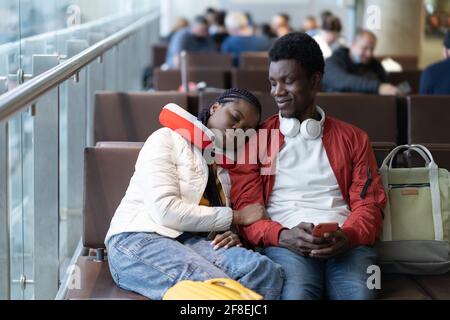 Un couple africain de touristes dans la zone d'attente du terminal de l'aéroport s'assoient, sieste avant l'enregistrement de départ Banque D'Images