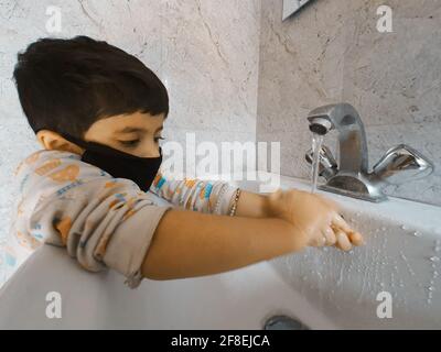 Enfants masqués se laver les mains pendant une pandémie de coronavirus. Le port et l'utilisation d'assainisseur du masque de lavage des mains sont recommandés par l'organisation mondiale de la santé. Banque D'Images