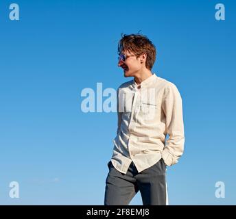 Vue latérale d'un jeune homme espagnol joyeux qui pose contre le ciel bleu Banque D'Images