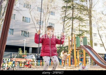 Une jeune fille en âge d'aller à l'école souriant joyeusement pendant que vous roulez sur le balançoires dans le parc Banque D'Images