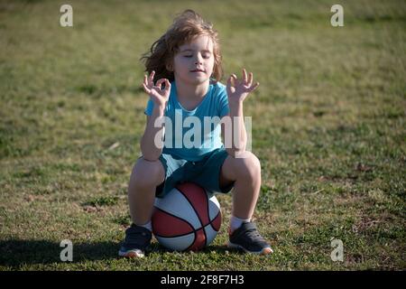 Un écolier assis sur le terrain de basket-ball et se détendre. Jeune sportif fatigué assis avec un ballon de basket à l'aire de jeux Banque D'Images