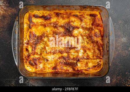 Lasagnes traditionnelles faites avec de la sauce bolognaise au bœuf haché recouverte de feuilles de basilic, sur un plateau de cuisson, sur fond rustique foncé, vue de dessus, plat Banque D'Images