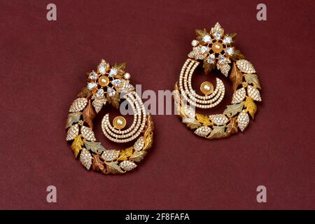Paire de boucles d'oreilles anciennes glamour et dorées sur fond rouge bijoux traditionnels indiens, boucles d'oreilles de mariée or bijoux de mariage, boucles d'oreilles vintage Banque D'Images