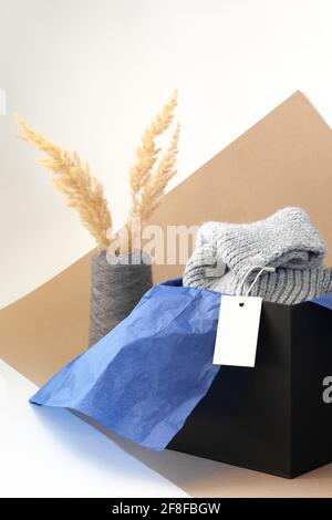 étiquette ou étiquette en papier blanc vierge pour la marque sur écharpe tricotée grise dans une boîte noire et bleue du papier de soie et de l'herbe de pampas séchée dans un fil de bobine vase Banque D'Images