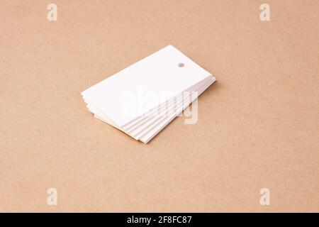 pile d'étiquettes de papier blanc vierge rectangulaires pour étiquettes de prix de vêtements sur fond de carton beige brun, isolées Banque D'Images