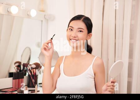 Belle jeune femme appliquant le maquillage près du miroir dans le dressing Banque D'Images