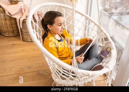Petite fille souriante, couchée sur un canapé confortable, appréciant de jouer en ligne sur un ordinateur tablette numérique. Accro à la technologie, heureux petit enfant utilisant