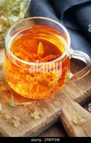 Tisane Linden avec des fleurs dans une tasse de verre sur bois rustique tableau avec fleur de lime herbe sèche à proximité, gros plan, boisson pour la détente, santé mentale, Banque D'Images