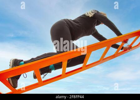 Mettre la femme en forme vêtements de sport entraînement extérieur sur l'escalier de pont d'arche métallique. Vue du dessous avec fond bleu ciel. Banque D'Images