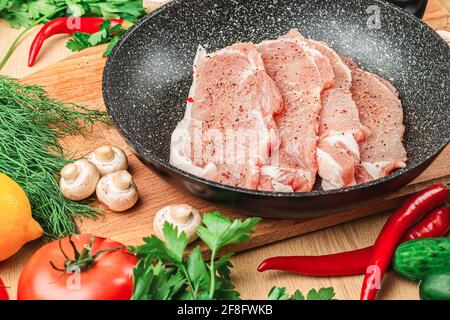 Viande de porc aux épices dans une casserole noire sur une planche de bois de près. Vue latérale et de dessus. À proximité se trouvent les champignons, la tomate, l'aneth, le persil, le poivre, citron Banque D'Images