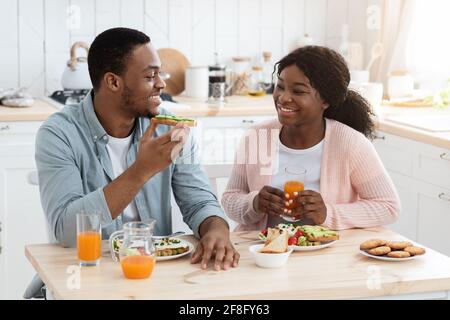 Joyeux conjoints afro-américains manger de la nourriture dans la cuisine et avoir Clavarder Banque D'Images