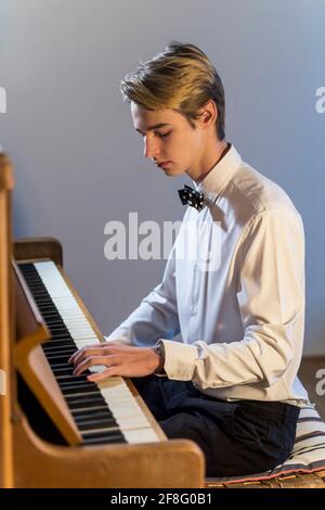 chemise blanche garçon avec noeud papillon joue du piano à la maison Banque D'Images