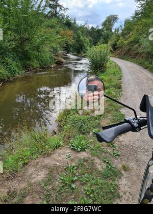 Cycliste photographié avec un smartphone. Homme caucasien sans casque de vélo prenant des photos de paysage. Activités de plein air. Tourisme prend la photo d'une rivière Banque D'Images