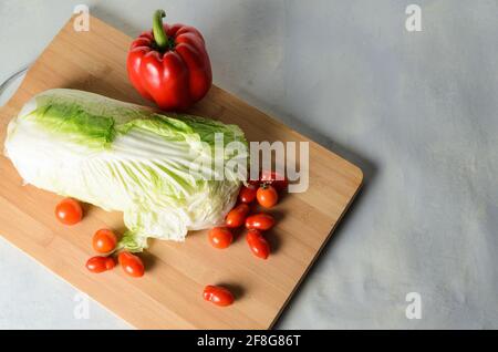 Légumes sur une planche à découper. Poivron rouge, tomates, chou pétsaï sur une planche. Mise au point sélective. Banque D'Images