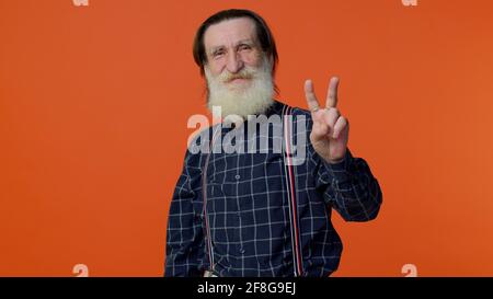 Homme barbu senior montrant le signe de la victoire, espérant le succès et la victoire, faisant le geste de paix et souriant Banque D'Images