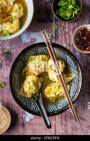 Plat de deux bols de soupe de wonton vegan maison avec tofu et brocoli servi sur une table en bois avec des baguettes avec de l'huile de chili croustillante Banque D'Images